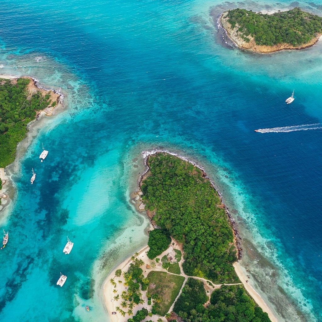 Soar over tropical islands where lush greenery meets turquoise waters, sandy beaches, and boats gently sailing by.